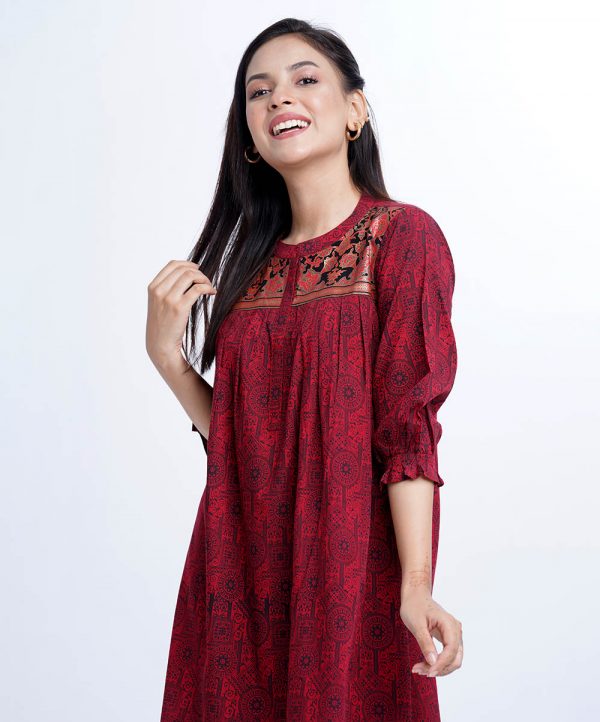 Red all-over printed ladies shirt in Viscose fabric. Features a mandarin collar with hook closure at the front and puff sleeves. Designed with pleats at the front. High-low hemline.