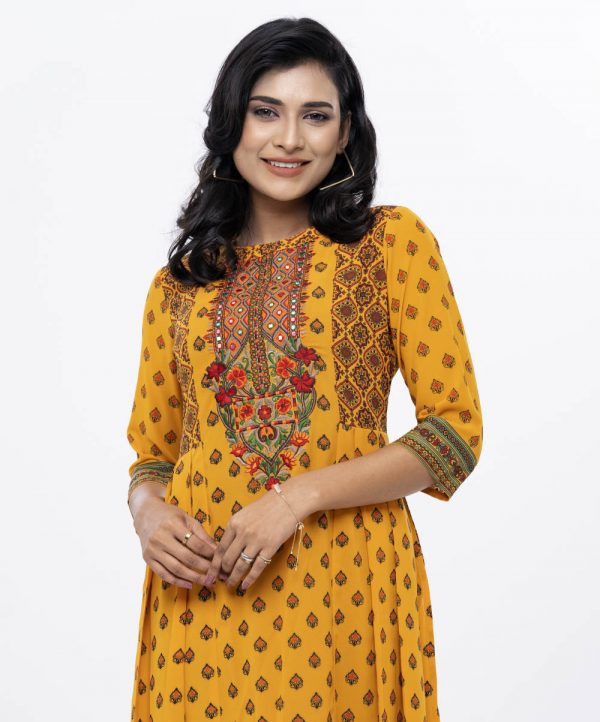 Yellow all-over printed A-line Tunic in Georgette fabric. Designed with a boat neck and three-quarter sleeves. Embellished with embroidery at the top front and pleats from the waistline. Single button opening at the back. Unlined.