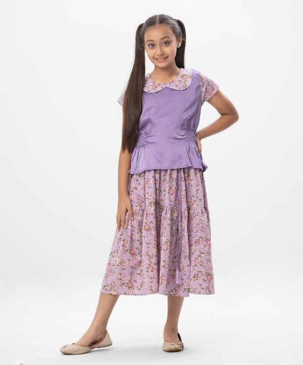 Purple Top-Skirt set in printed Georgette fabric. The top features a round neck with a baby collar and cap sleeves. Designed with smoky-waist. Paired with a printed georgette skirt as the bottom.