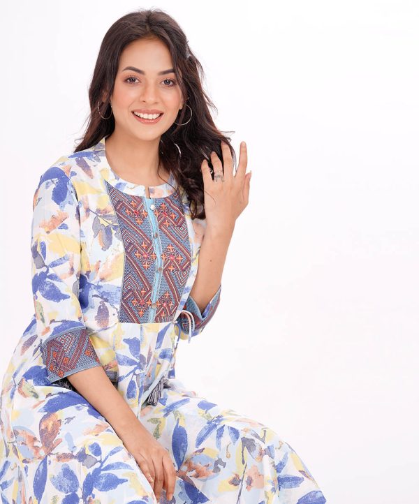 White pattern A-line Tunic in printed Georgette fabric. Features a band collar with hook closure at the front and three-quarter sleeves. Embellished with fancy buttons and karchupi at the top front. Printed patch attachment at the cuffs. Unlined.