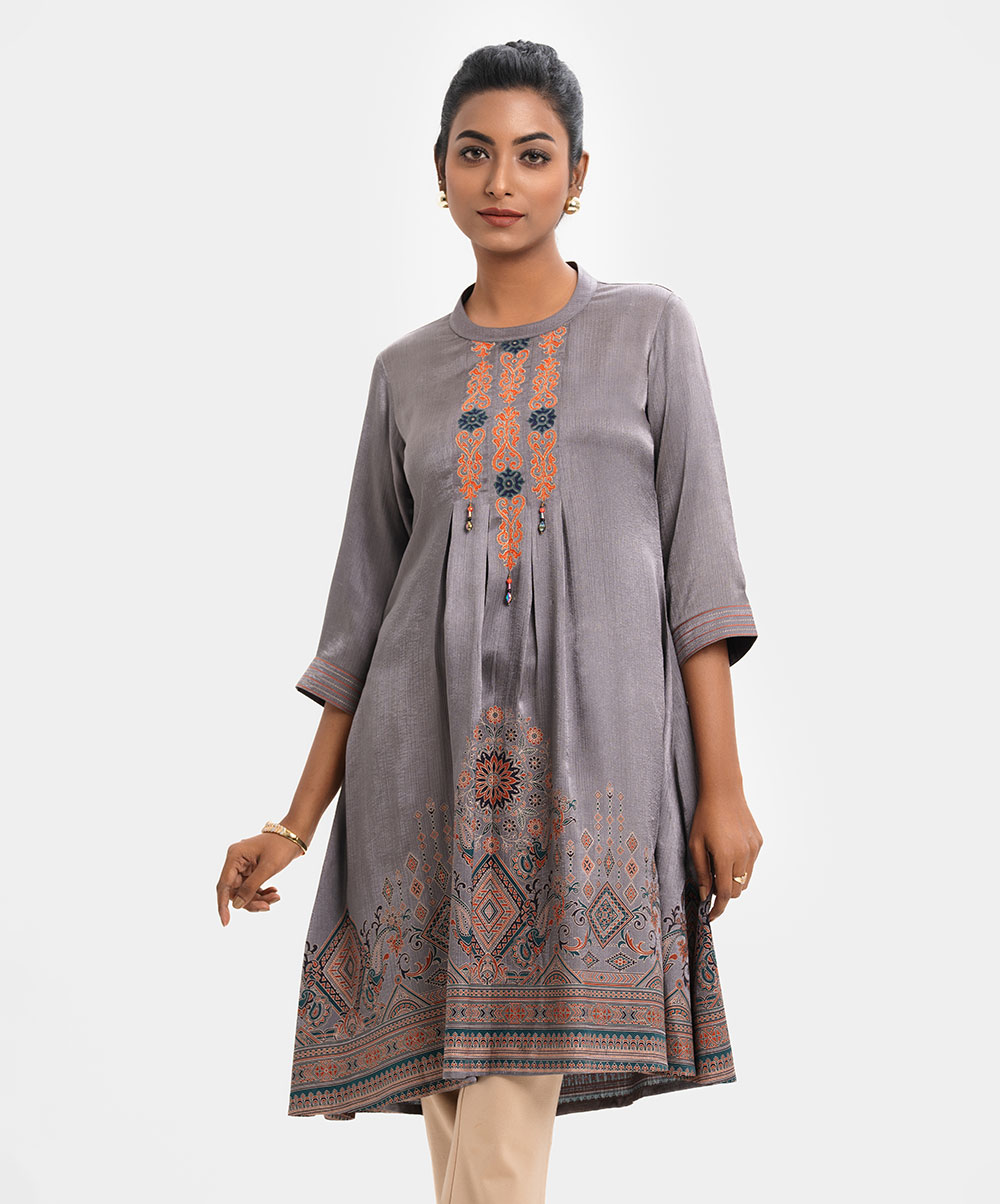 Women's A-line tunic in textured georgette fabric. Mock neck, three-quarter sleeves. Embroidery with tassels and box pleated at front. Print detail at hemline. Ash Georgette A-line Tunic